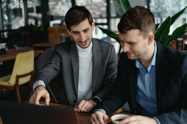 Two businessmen pointing laptop screen while discussing