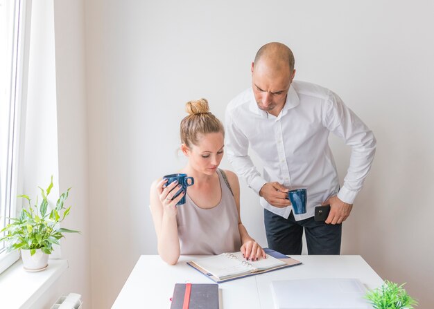 Free photo two businesspeople holding coffee cup looking at diary