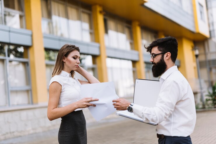मुफ़्त फोटो two businesspeople looking at document standing outside the office