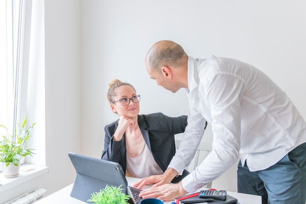 Two businesspeople looking at each other while working on laptop