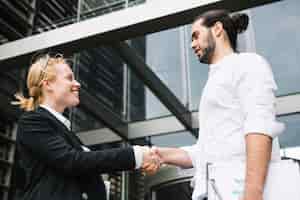 Бесплатное фото Двое бизнесменов стоят возле офисного здания и пожимают друг другу руки