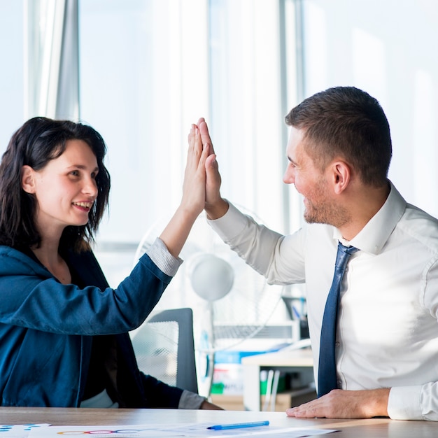 Two businesswoman and businessman giving hi-five across the table