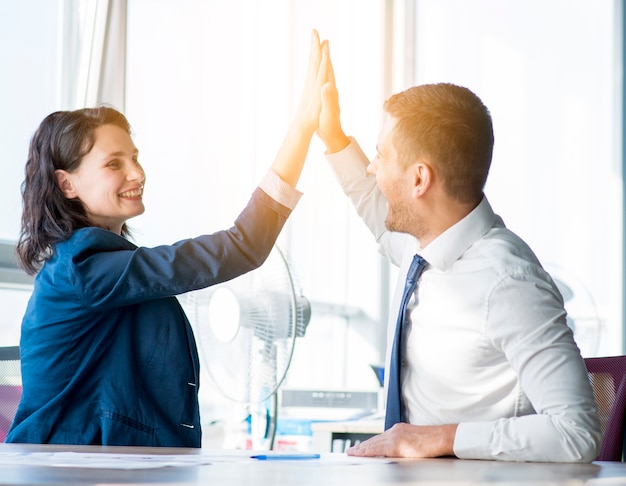 Two businesswoman and businessman giving hi-five in the office