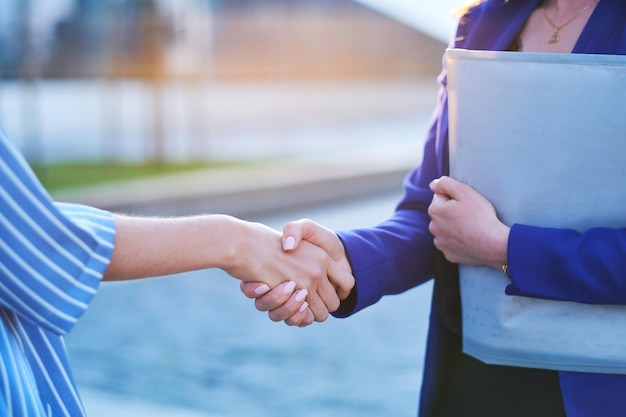 Two busy businesswomen have unformal meeting outside, they are greeting one each other with handshake.