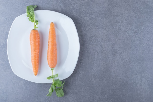 Две моркови в тарелке на мраморной поверхности.