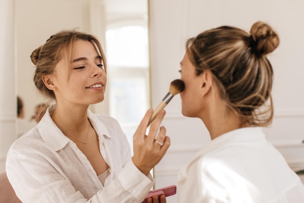 Two caucasian female models undergo cosmetic procedures, apply blush while having well-groomed skin. Rituals of female beauty, concept