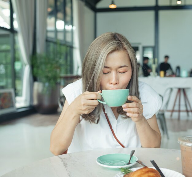 Two cheerful and beautiful girls are sitting together near the table and watching something on the phone. they look relaxed and happy. also girls are enjoying the time spending together.