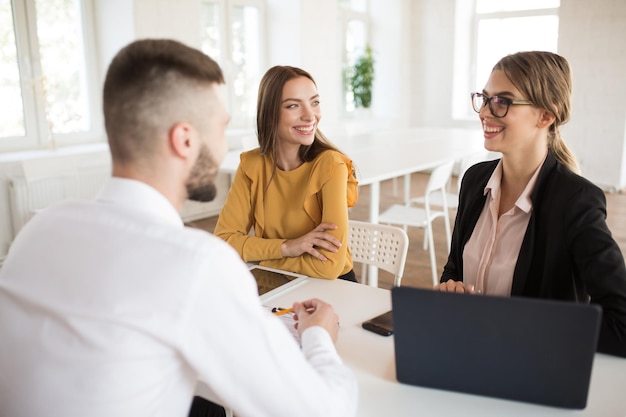 Two cheerful business women happily talking with male applicant for work Young smiling employers spending job interview in modern office