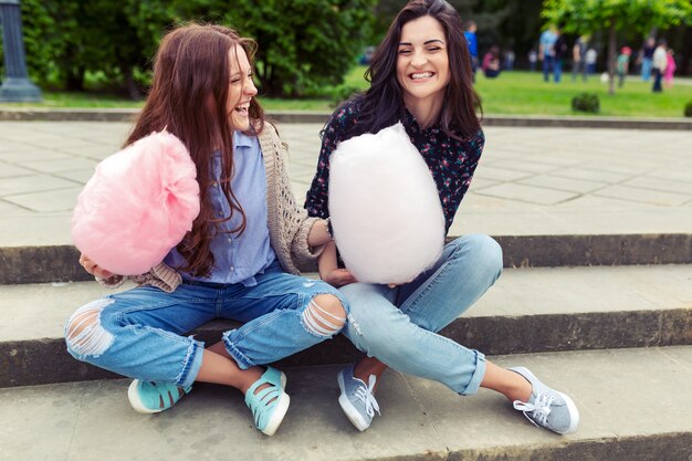 Two cheerful girls having fun with cotton candy outdoor