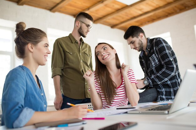 Two cheerful girls joyfully talking while spending time in modern office with colleagues on background Group of creative people working together