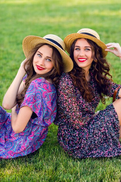 two cheerful twins sitting on green meadow and enjoy time together.