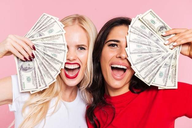 Free photo two cheerful women covering their half faces and looking at the camera with open mouth over pink