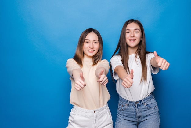 Two cheerful women thumbs up isolated on blue wall. People lifestyle concept. Mock up copy space. Showing thumbs up