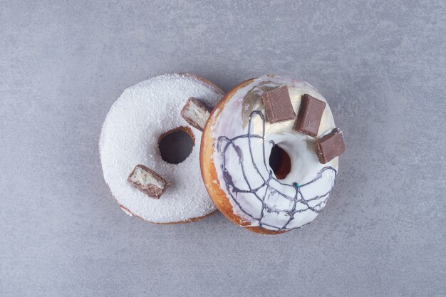 Two chocolate-adorned donuts on marble surface