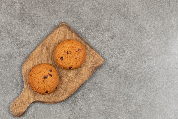 Two chocolate cookies on wooden board.