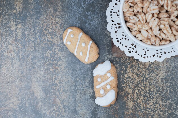 Two Christmas cookies and bowl of sweet peanuts on marble surface. High quality photo