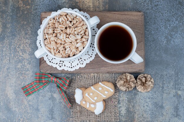 木の板に2つのクリスマスクッキー、お茶と甘いピーナッツ。高品質の写真