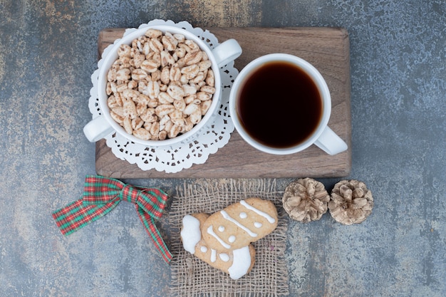 Two Christmas cookies, cup of tea and sweet peanuts on wooden board. High quality photo