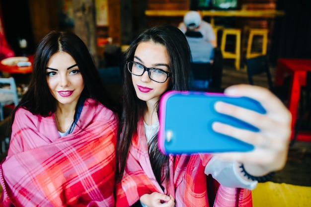 two close girlfriends want to make a selfie in the cafe on memory