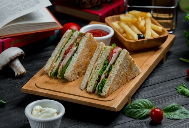 Two club sandwiches with cheddar and bacon served with sauces and fries