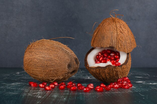 Two coconuts with pomegranate on marble surface
