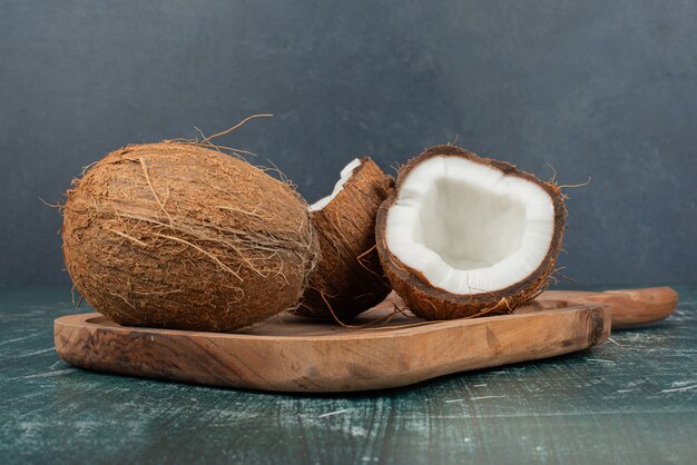 Two coconuts on wooden board on marble surface