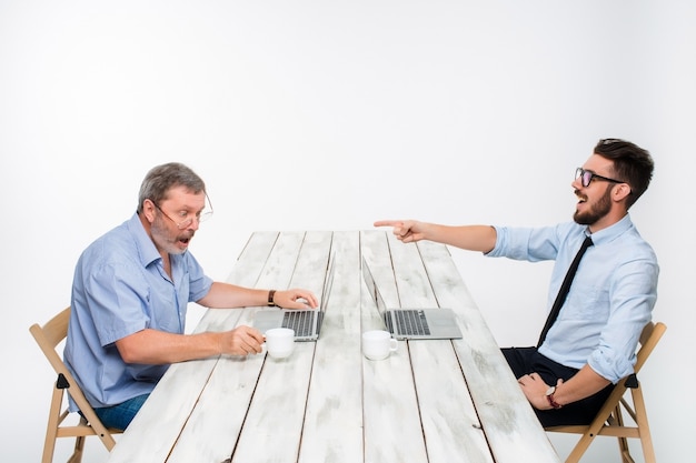 The two colleagues working together at office on white  background. One man are looking at the computer screens. another man laughing at other