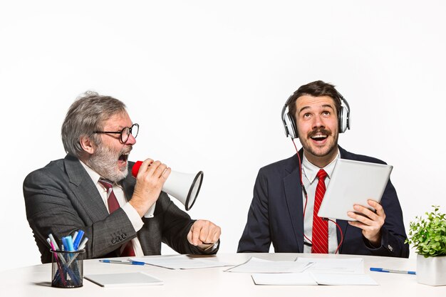 The two colleagues working together at office on white background. one man shouting through a megaphone - other in headphones can not hear nothing