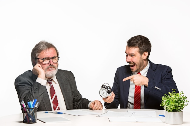 Foto gratuita i due colleghi che lavorano insieme in ufficio su sfondo bianco. discutono attivamente ed emotivamente i piani attuali con l'orologio