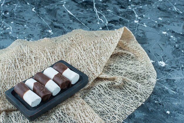 Two-color candies on a wooden plate on a tablecloth , on the blue table. 