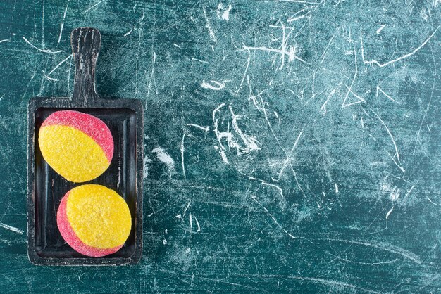 Two colored cookies on black cutting board.