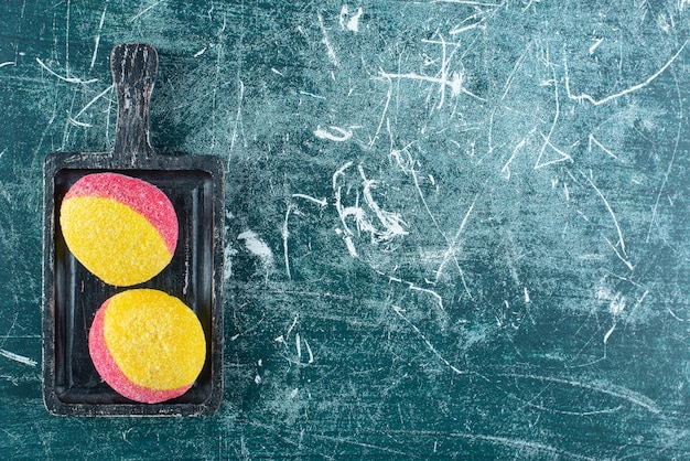 Two colored cookies on black cutting board.