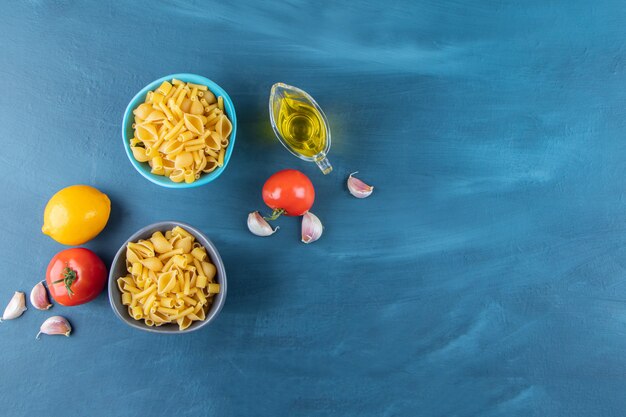 Two colorful bowls of raw pasta with fresh red tomatoes and one whole lemon . 