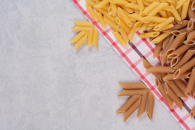 Two colors of raw pasta on striped tablecloth.