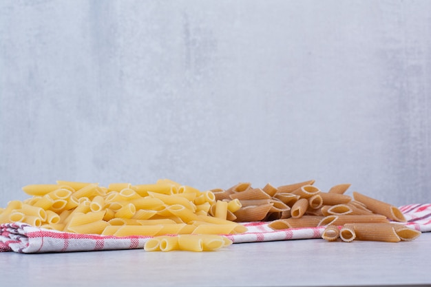 Two colors of raw penne pasta on striped tablecloth
