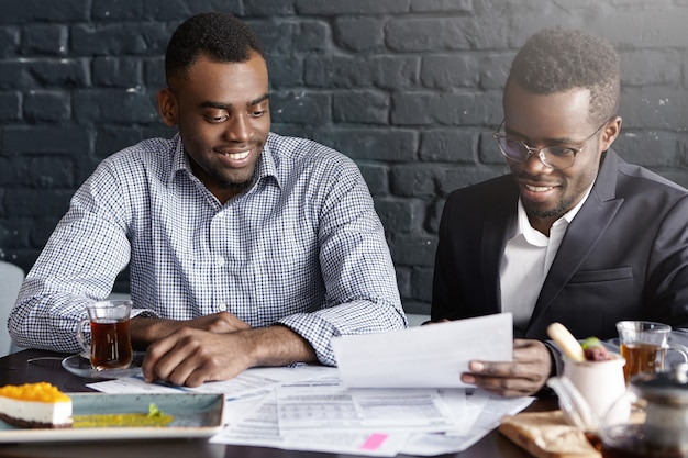 Two confident dark-skinned executives smiling happily after having signed profitable deal