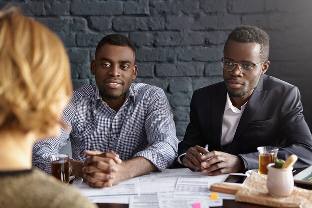 two confident and successful african hr managers interrogating young female candidate during job interview