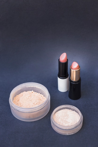 Two container of beige blusher powder and lipsticks on gray backdrop