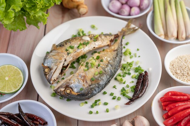 Two cooked mackerel, placed in a white dish, sprinkled with spring onions.