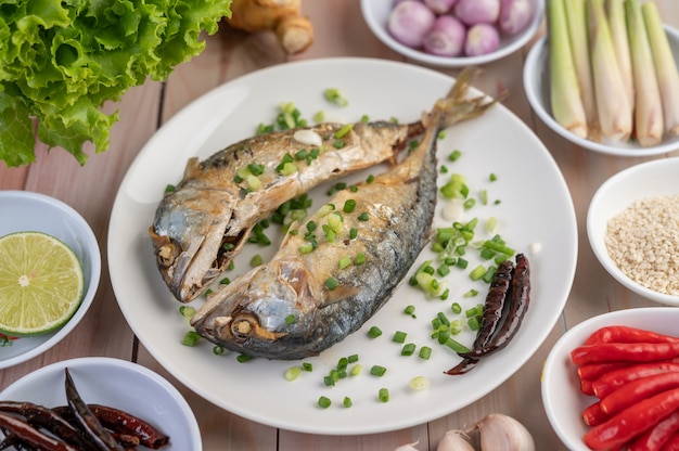 Two cooked mackerel, placed in a white dish, sprinkled with spring onions.