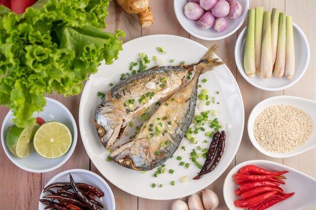 Two cooked mackerel, placed in a white dish, sprinkled with spring onions.