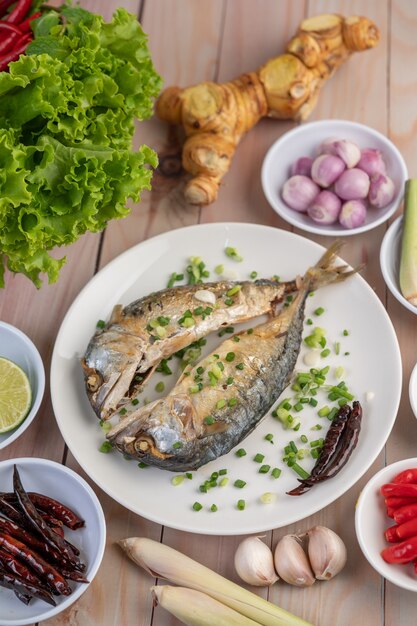 Two cooked mackerel, placed in a white dish, sprinkled with spring onions.