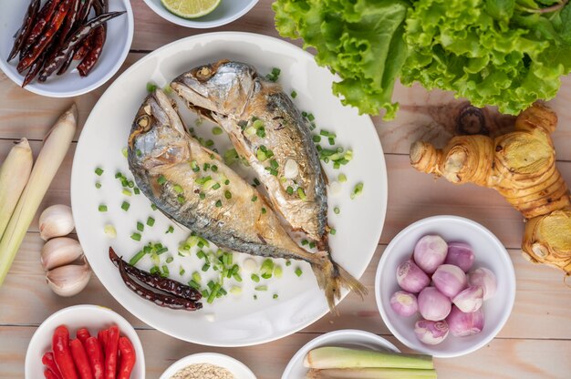 Two cooked mackerel, placed in a white dish, sprinkled with spring onions.