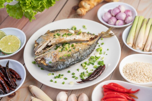 Two cooked mackerel, placed in a white dish, sprinkled with spring onions.