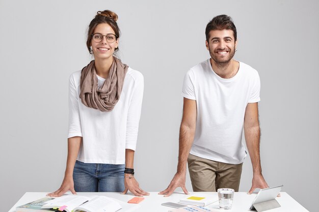 Two coworkers stand in modern office at table with documents and tablet