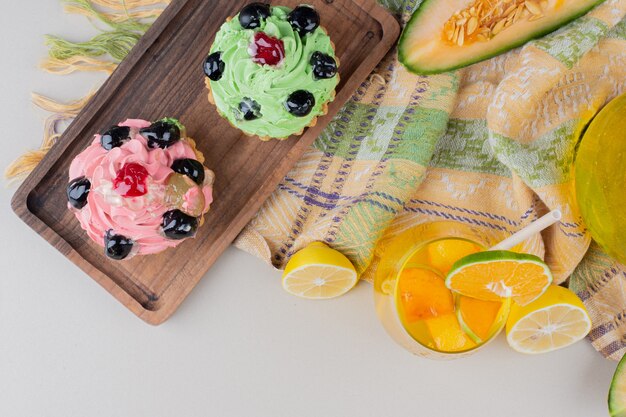 Two creamy cupcakes on wooden board.