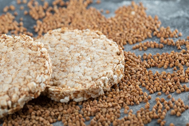 Two crispbread and uncooked buckwheat on marble surface