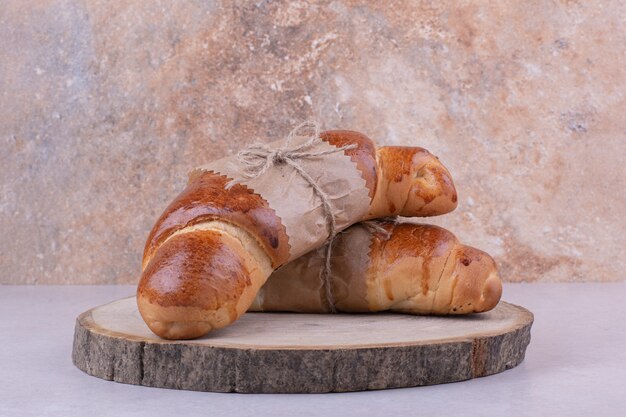 Two croissant buns in paper wrap on wooden board.