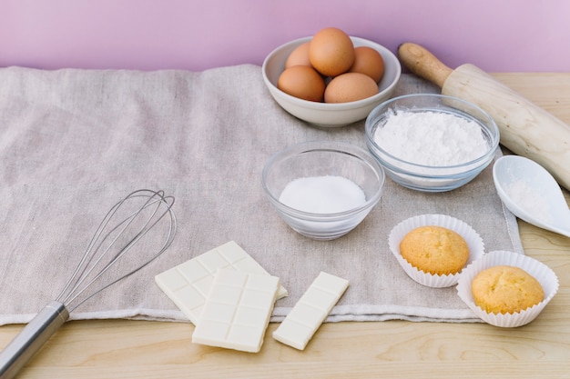 Two cupcakes with ingredients on tablecloth over the desk