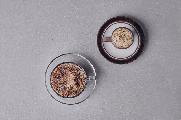 Two cups of cappuccino on grey background.